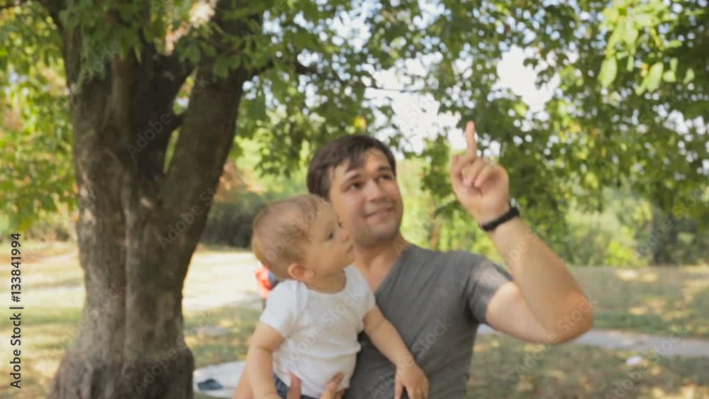 Portrait of happy young father cuddling his baby son at park under tree Portrait of happy young father cuddling his baby son at park under tree