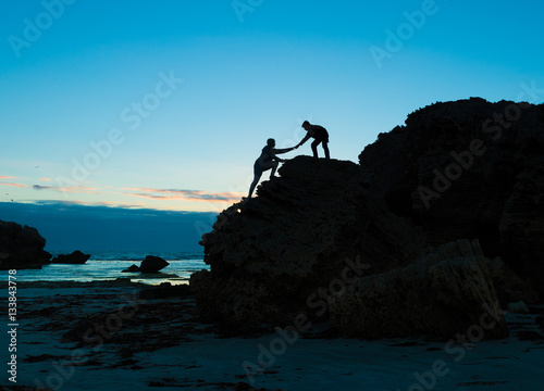 Two people climbing up the cliff teamwork help to succsess
