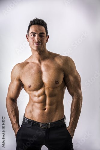 Handsome shirtless muscular man with elegant pants, standing, on light background