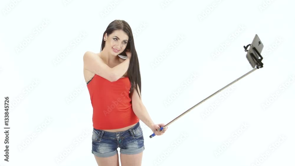 Long-haired brunette makes selfie using a monopod. Studio. White background Long-haired brunette makes selfie using a monopod. Studio. White background