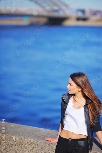 Portrait profile of young beautiful woman with tousled in the wind long hair, standing on the waterfront on the background the blue waters of the Neva.