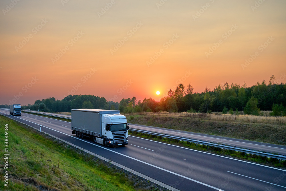 White trucks driving on the asphalt highway in the landscape at sunset