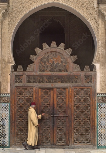 Man in traditional clothing leaving temple through main doors. 
