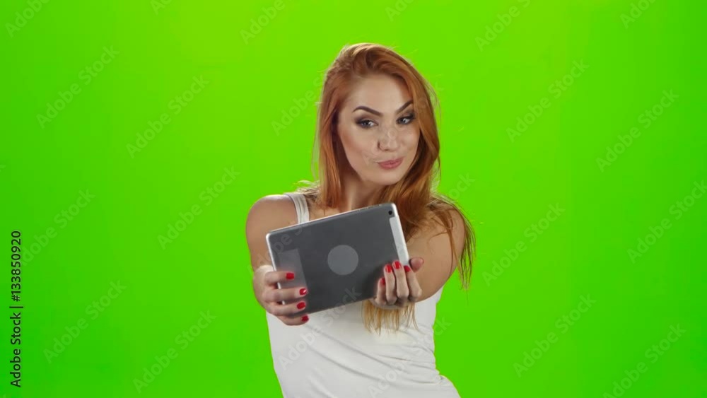 Redheaded model grimaces on camera a tablet. Green screen studio Redheaded model grimaces on camera a tablet. Green screen studio