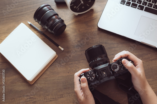 Camera on hand.Photographer workplace, Camera,Laptop,Memo on wooden desk.