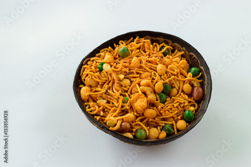 Traditional famous Indian snack namkeeni in coconut shel cup. A mixture of roasted nuts, puffed rice, dried fruits and roasted grams, seasoned with various spices. Light background