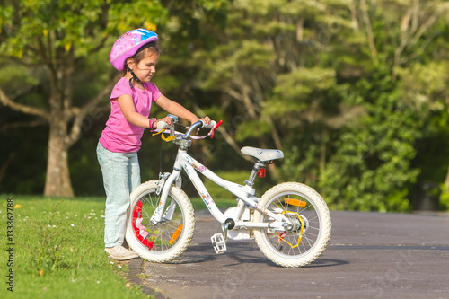 outdoor portrait of young happy child girl riding a bike in park