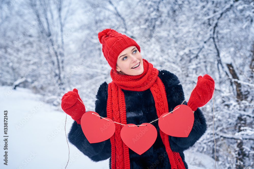Love and valentines day concept. Smiling woman holding garland of three red paper hearts shape - blank copy space for letters or text, looking up over winter landscape Love and valentines day concept. Smiling woman holding garland of three red paper hearts shape - blank copy space for letters or text, looking up over winter landscape