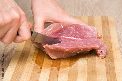 Man's hand with a knife cuts the meat on the wooden board in the kitchen. Cooking at home. Healthy eating and lifestyle.