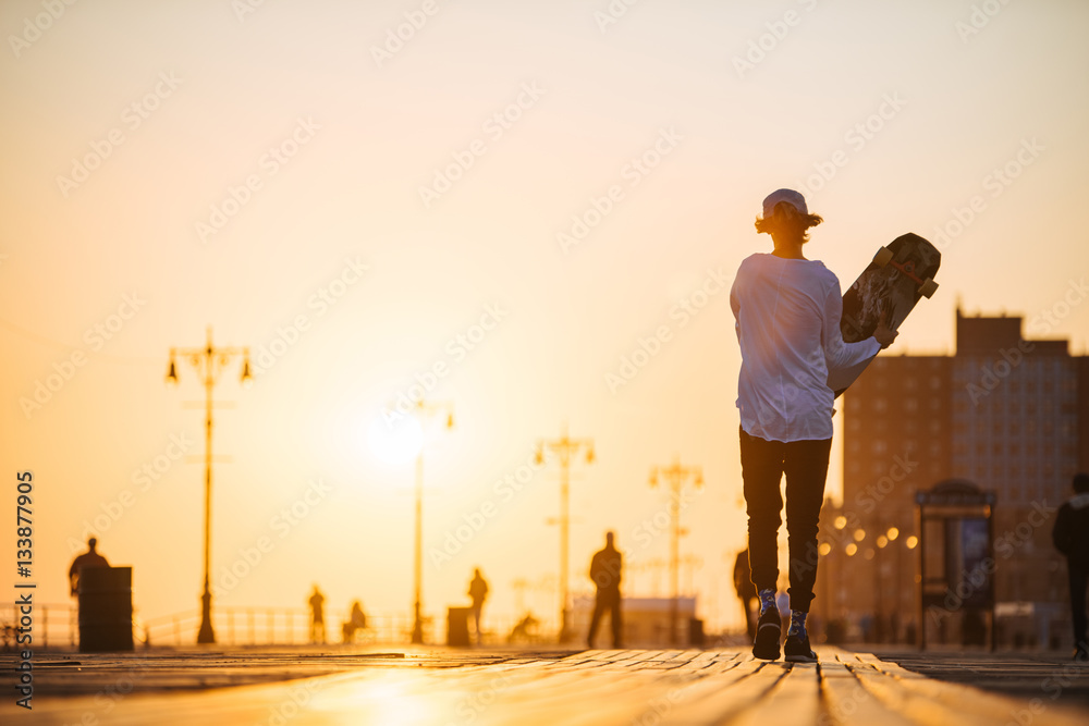 Young hipster man walking with longboard in hands on the boardwalk outside Young hipster man walking with longboard in hands on the boardwalk outside