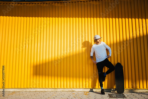 Young hipster guy portrait with longboard stranding at yellow wall photo