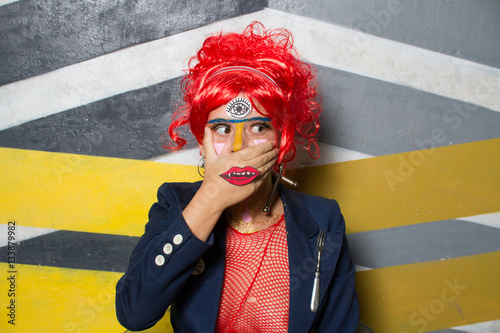Retrato de chica joven con estética punk y post-punk (tribu urbana futurista) con peluca roja y con la cara pintada haciendo gestos provocativos