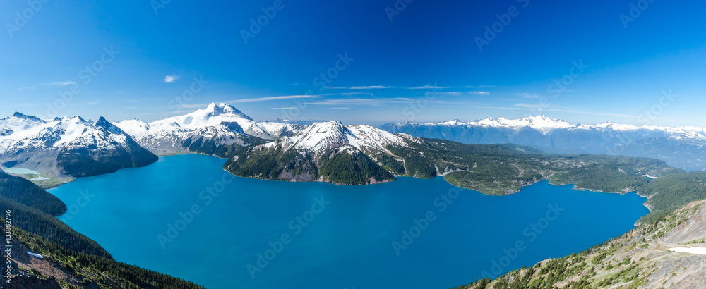 Panoramic wide scenery from Panorama Ridge peak with view over whole Garibaldi lake and surrounding mountains covered in snow during sunny summer day, Whistler, British Columbia, Canada.