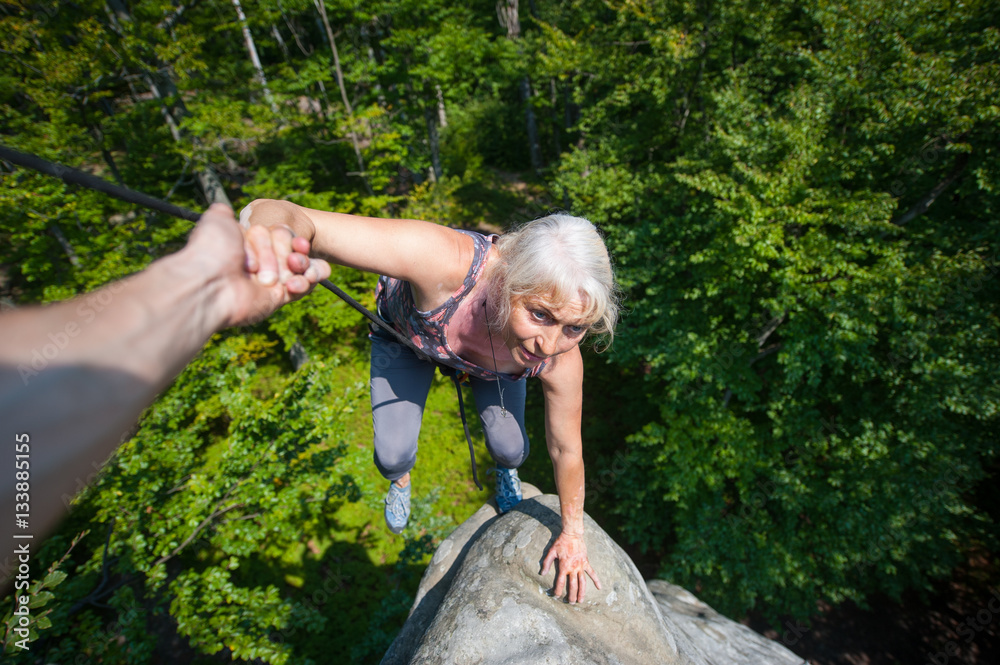 Older woman climbing on high rock, her male partner giving her a