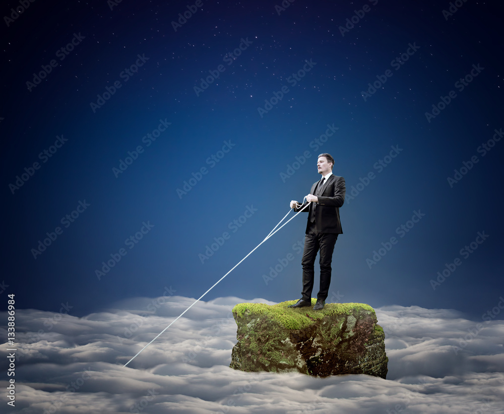 Businessman Holding a Rope Standing on Rock Above Clouds - Company Management Concept Businessman Holding a Rope Standing on Rock Above Clouds - Company Management Concept