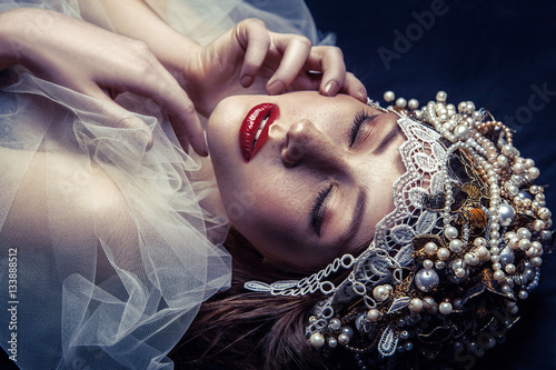 Картината върху платно fashion beauty portrait of young beautiful young woman with makeup and freckles on her face and pearl headpiece on her head and white tulle in front of her face on dark blue background