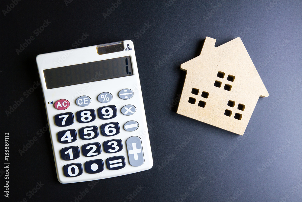 Wooden house toy and calculator on black background with copy sp Wooden house toy and calculator on black background with copy sp