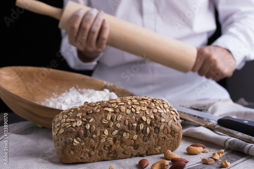 Whole grain bread put on kitchen napkin decorated with almond with a chef holding dough roller at the background.