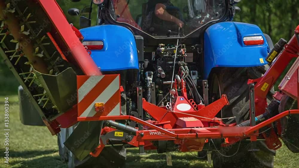 Grass cutting machinery is slowly folding together. A tractor is standing still in the middle of the field.
Grass cutting machinery is slowly folding together. A tractor is standing still in the middle of the field.