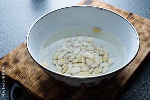 Canvas-taulu Large white beans soaking in water on a dark wooden cutting board