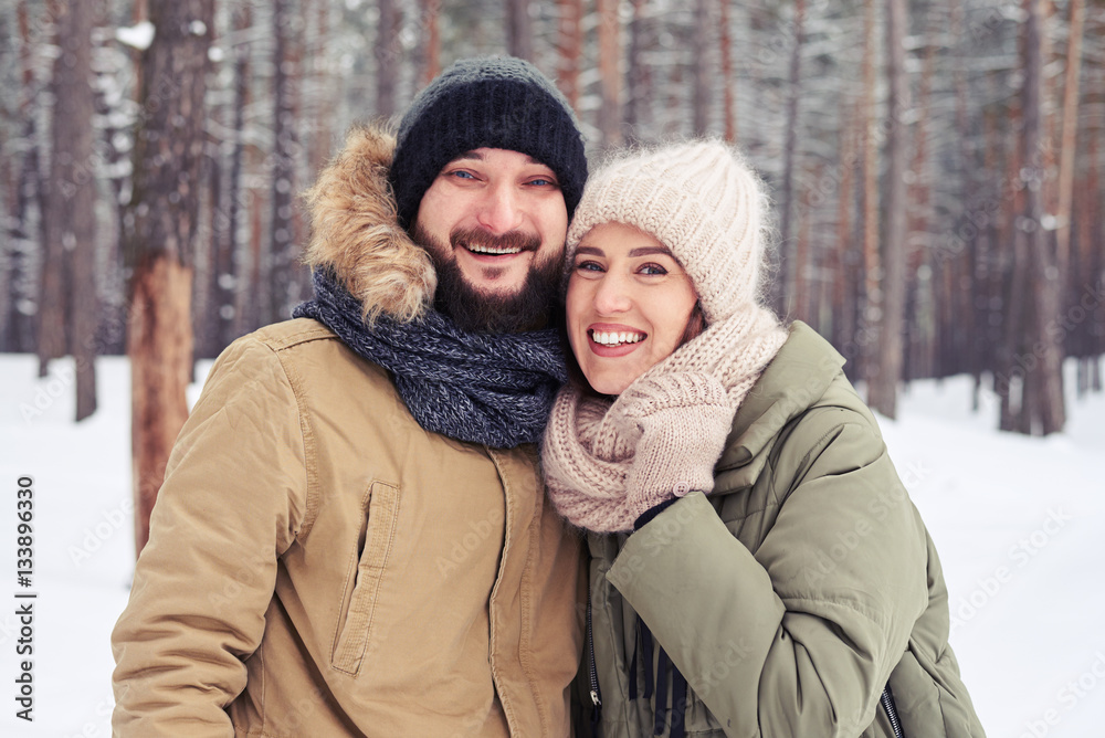 Fototapeta premium Cheer couple embracing over a picturesque wintry forest