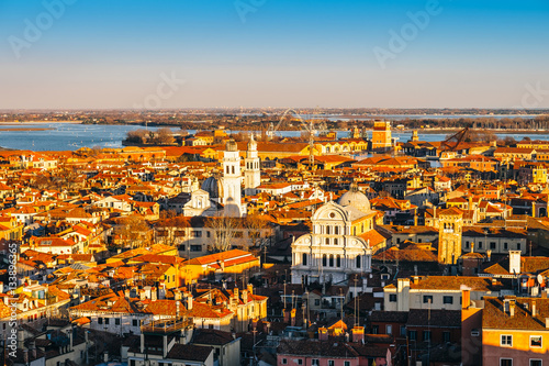 Aerial view of Venice, Italy, at sunset with rooftops of buildings and warm sunlight.