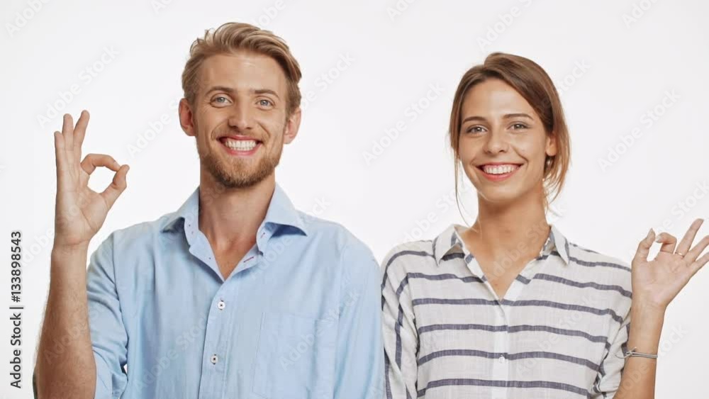 Successful Caucasian couple standing back to back on white background. Then turning and showing ok to camera with one hand in slowmotion Successful Caucasian couple standing back to back on white background. Then turning and showing ok to camera with one hand in slowmotion