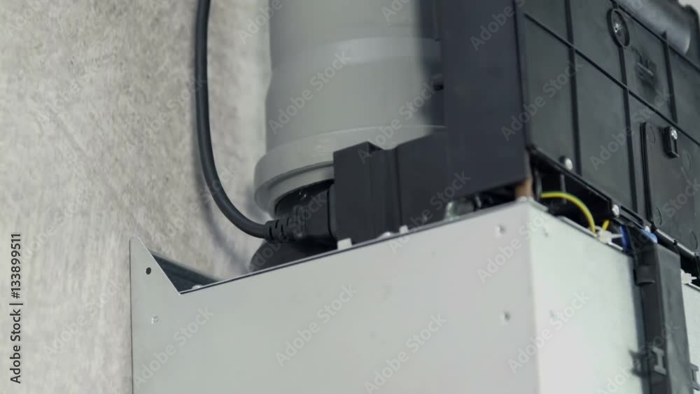 A young woman plugs in a black cable into a device which is standing on a kitchen ventilator.
A young woman plugs in a black cable into a device which is standing on a kitchen ventilator.
