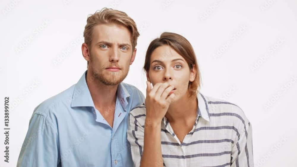 Young Caucasian pair looking at camera in slowmotion with suspicion and disapproval on white background Young Caucasian pair looking at camera in slowmotion with suspicion and disapproval on white background