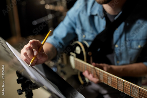 man with guitar writing to music book at studio photo