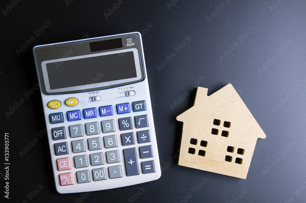 Wooden house toy and calculator on black background with copy sp Wooden house toy and calculator on black background with copy sp