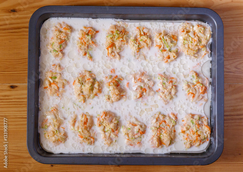 Raw lazy cabbage rolls in pan for baking drenched with sour cream.