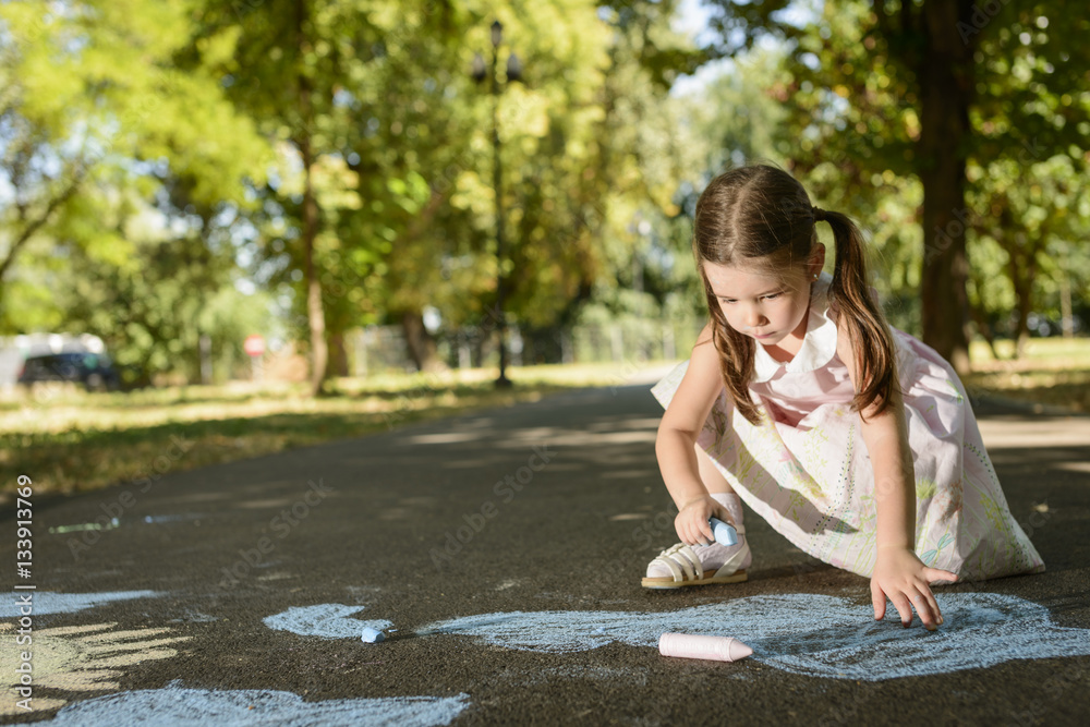 Little girl drawing on asphalt with chalk in a sunny summer day. Concept of child imagination Little girl drawing on asphalt with chalk in a sunny summer day. Concept of child imagination