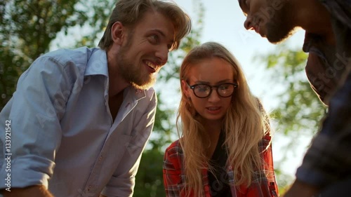 Caucasian bearded male with blonde female discussing with dark-skinned man plan sitting in park with felt-pens. Tarantino view in slowmotion photo