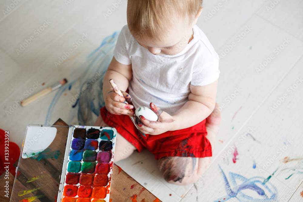 Fotografie smutty kid paints eggs on light background,
