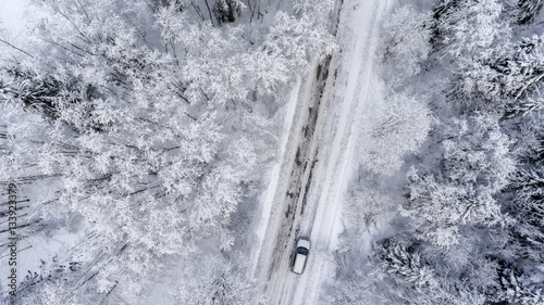 Suv driving in white snowy evergreen forest on slipery asphalt road. Aerial view from drone © Kekyalyaynen