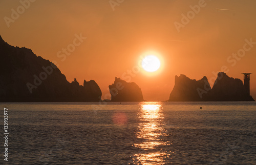 sun setting behind rock and lighthouse 