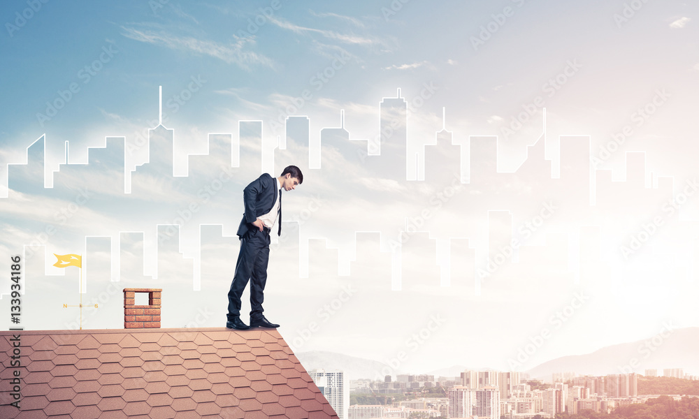 Businessman looking down from roof and modern cityscape at backg Businessman looking down from roof and modern cityscape at backg