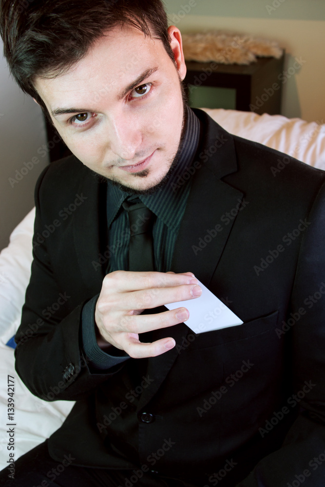 Hombre joven y guapo con un traje de chaqueta negro sacando una tarjeta de  visita de su bolsillo Stock Photo | Adobe Stock