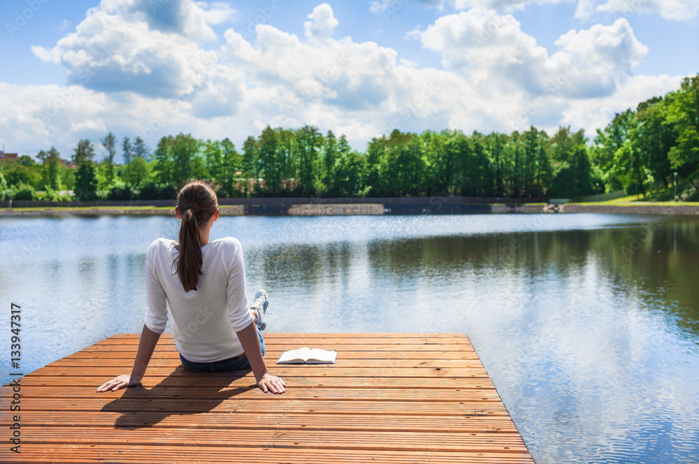 Woman relaxing by a beautiful lake.  - obrazy, fototapety, plakaty 