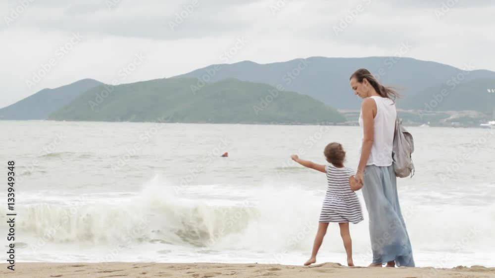 Mother with little daughter walking along the sea in bad weather Mother with little daughter walking along the sea in bad weather