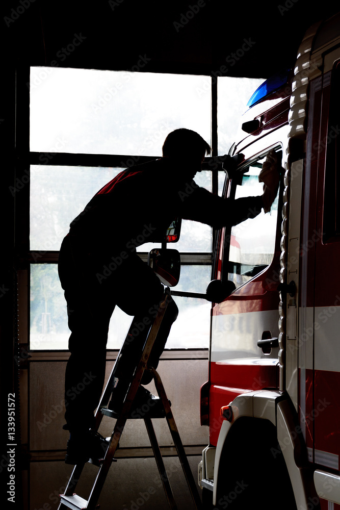 Fototapeta premium Firefighter cleans firetruck. Maintenance of fire equipment. Life at the fire station.