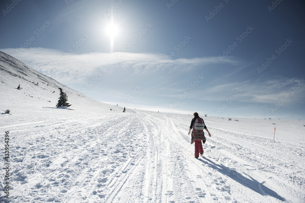 Rear view of woman walking on snow covered field against sky on sunny day Rear view of woman walking on snow covered field against sky on sunny day