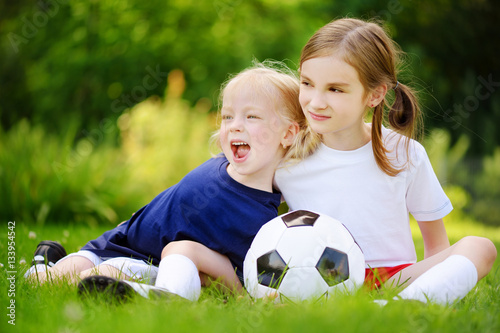 Two cute little sisters having fun playing a soccer game