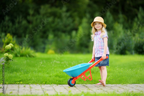Adorable little girl having fun with a toy wheelbarrow