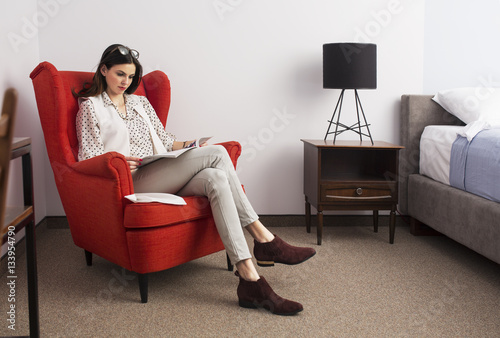Woman reading magazine while sitting on armchair