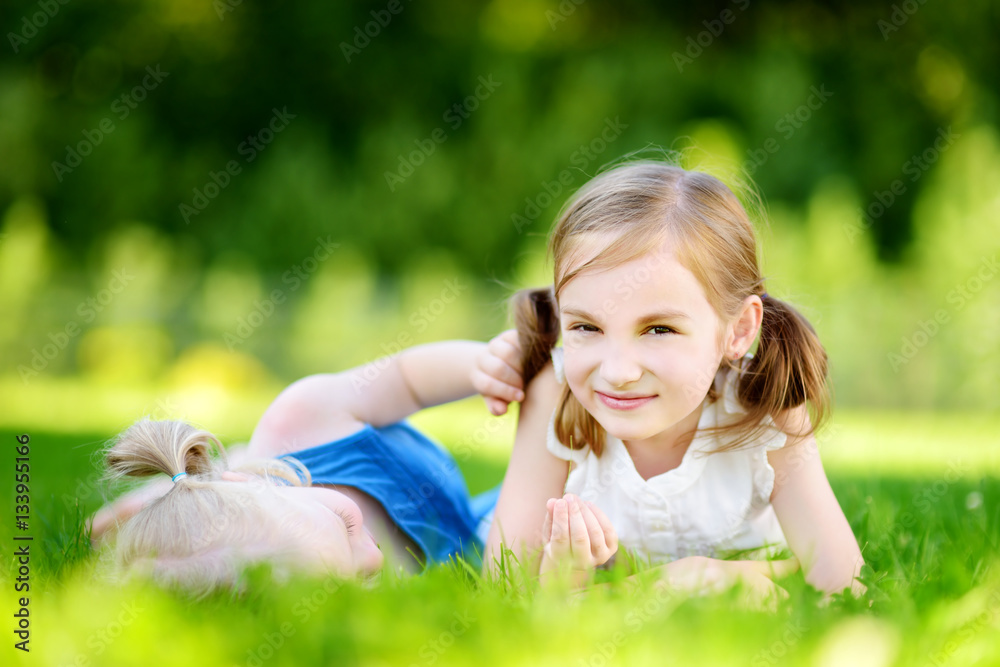 Two cute little sisters having fun together on the grass Two cute little sisters having fun together on the grass