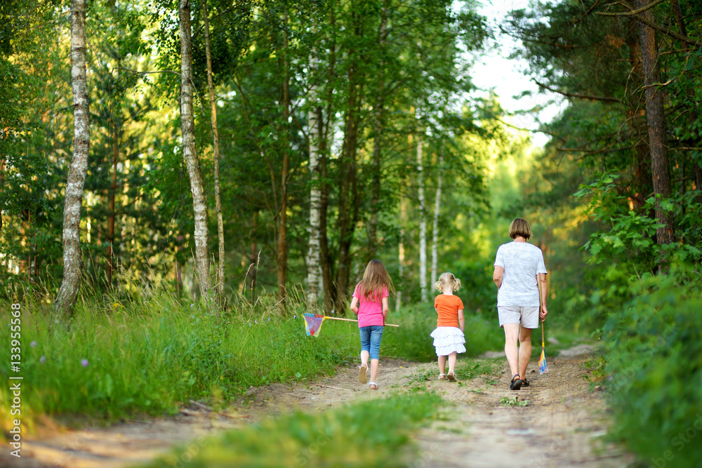 Fototapeta premium Two vute little sisters hiking in a forest with their grandmother