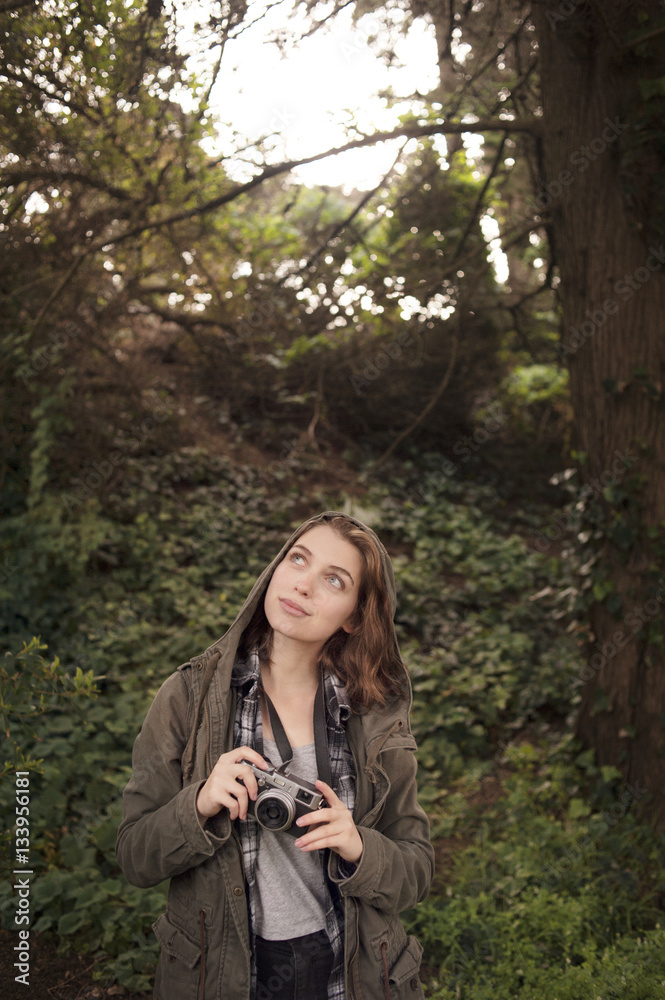 Thoughtful young woman holding camera in forest Thoughtful young woman holding camera in forest
