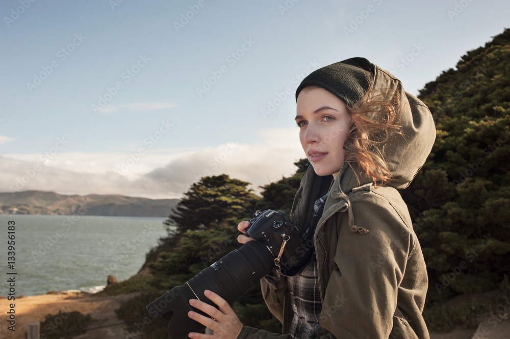 Thoughtful female photographer holding camera while standing outdoors Thoughtful female photographer holding camera while standing outdoors